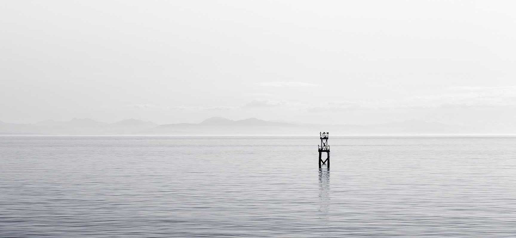 Ein einsamer Pfahl im stillen Wasser, fast verborgen im Nebel